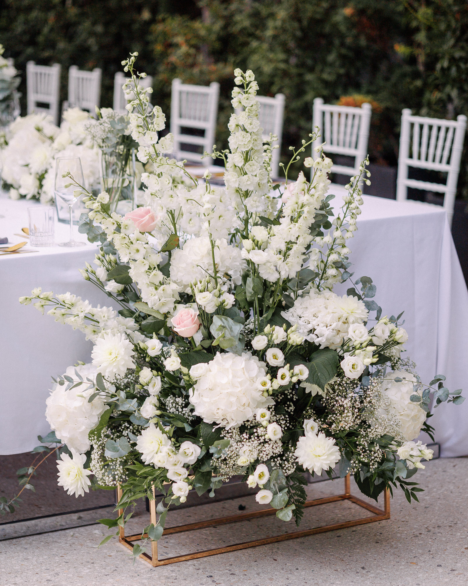 Outdoor wedding dinner at a long table with white floral arrangements in the garden